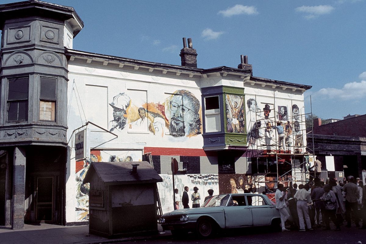 Optima Lakeview® Apartments in Chicago, IL Artists from the Chicago Public Art Group paint a mural as a crowd watches; a vintage car marks over 50 years of public art.