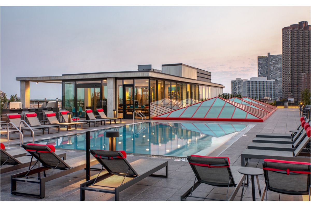 Optima Lakeview® Apartments in Chicago, IL Enjoy stunning evenings on the Sky Deck, featuring a rooftop pool, lounge chairs, red accents, and city views at sunset.