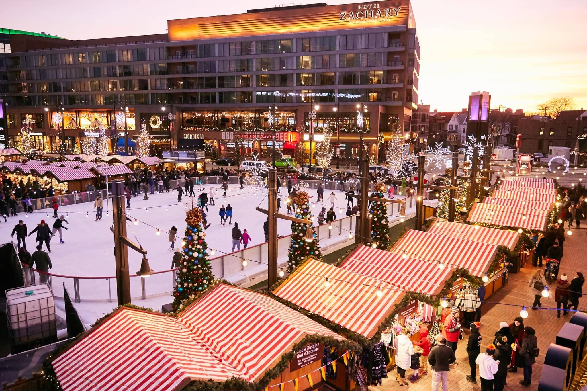 Optima Lakeview® Apartments in Chicago, IL Festive outdoor ice rink and Christmas market stalls with lights at sunset in front of a large hotel.