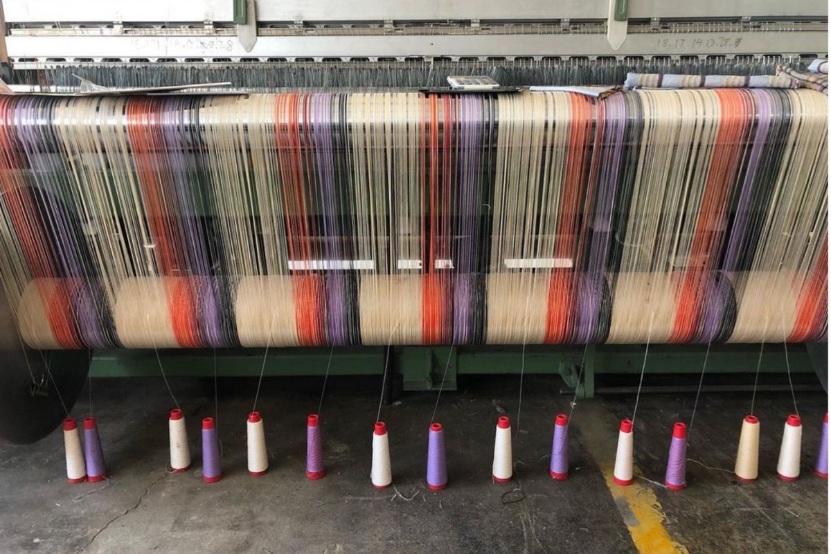 Optima Lakeview® Apartments in Chicago, IL A weaving loom at The Weaving Mill in Chicago with threads in white, orange, purple, and red, and spools hanging below.