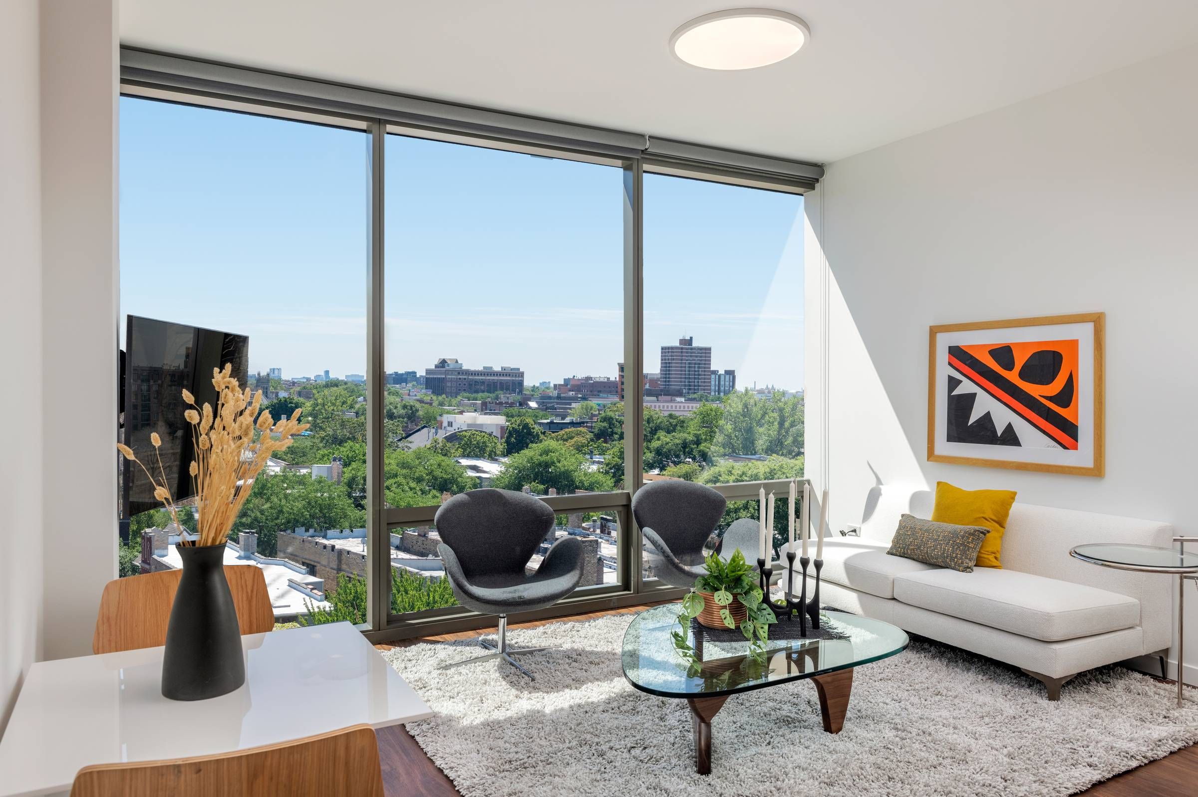 Optima Lakeview® Apartments in Chicago, IL Modern living room with large windows, city view, white sofa, glass coffee table, and contemporary decor.
