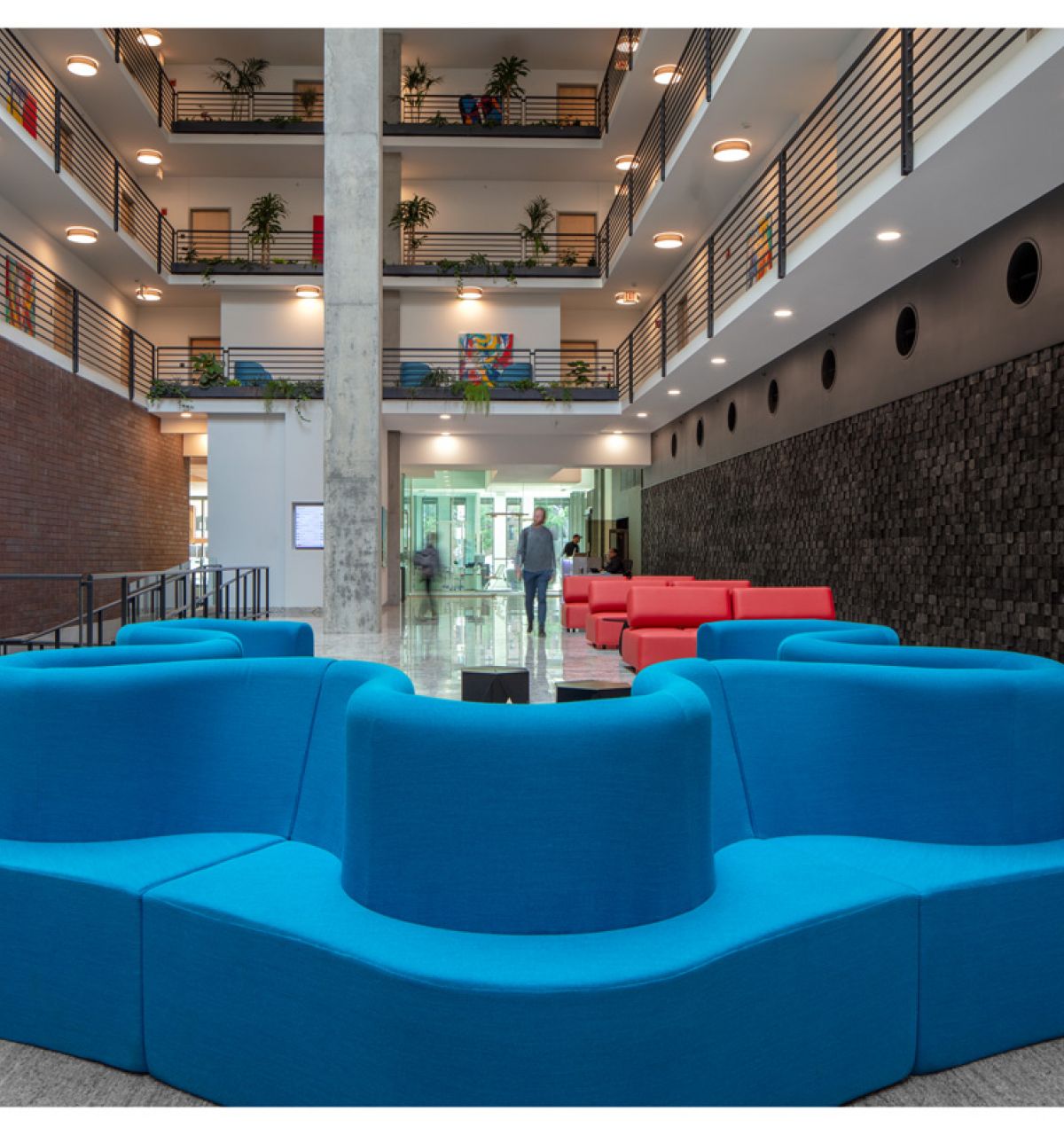 Optima Lakeview® Apartments in Chicago, IL Modern atrium with Optima's lobbies-inspired blue seating, red sofas, and striking multi-story walkways above.