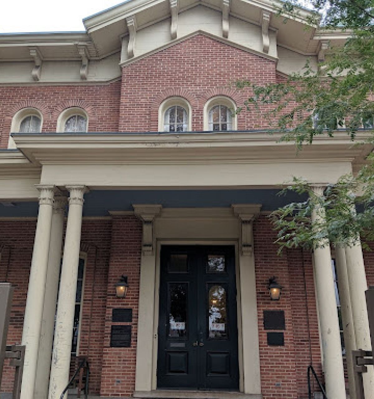 Optima Lakeview® Apartments in Chicago, IL A historic brick building with columns and arched windows, Hull House in Chicago was a center for social reform, partially shaded by trees.