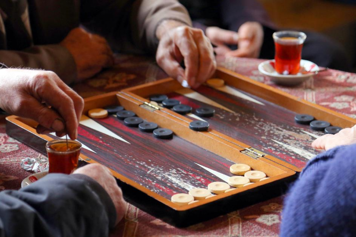 Optima Lakeview® Apartments in Chicago, IL Three people enjoy a fun game of backgammon over tea, their hands moving pieces across a trending wooden board.