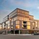 Optima Lakeview® Apartments in Chicago, IL Modern multi-story building with large glass windows on a city street at sunset, reflecting the sky.