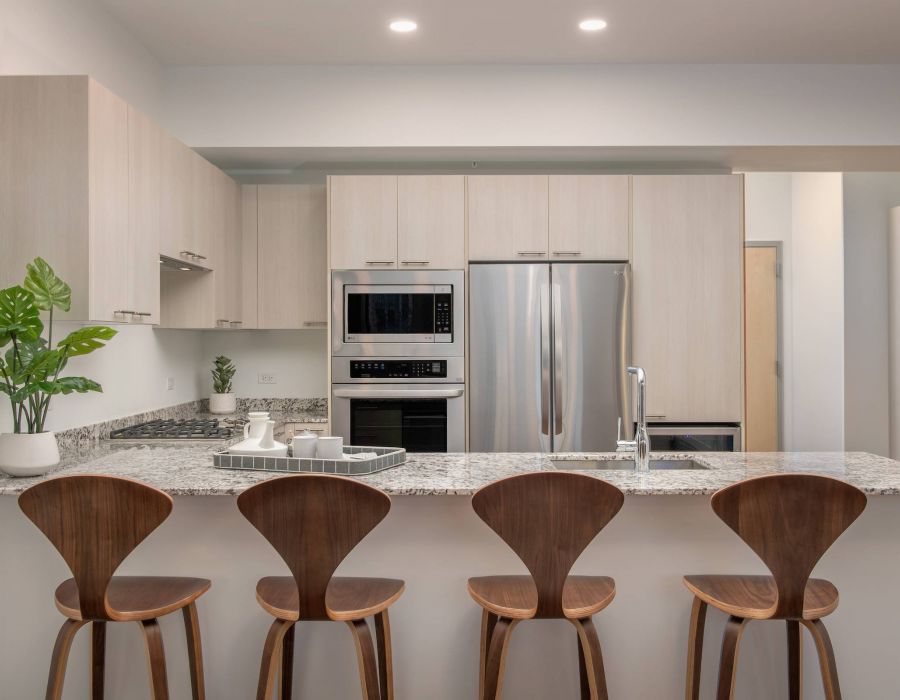 Optima Lakeview® Apartments in Chicago, IL Modern kitchen with light wood cabinets, granite island, four wooden stools, and stainless steel appliances.