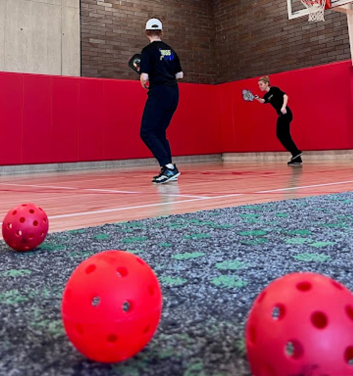 Optima Lakeview® Apartments in Chicago, IL Two people play pickleball in a gym, fostering connection on a carpeted surface with red balls in the foreground.