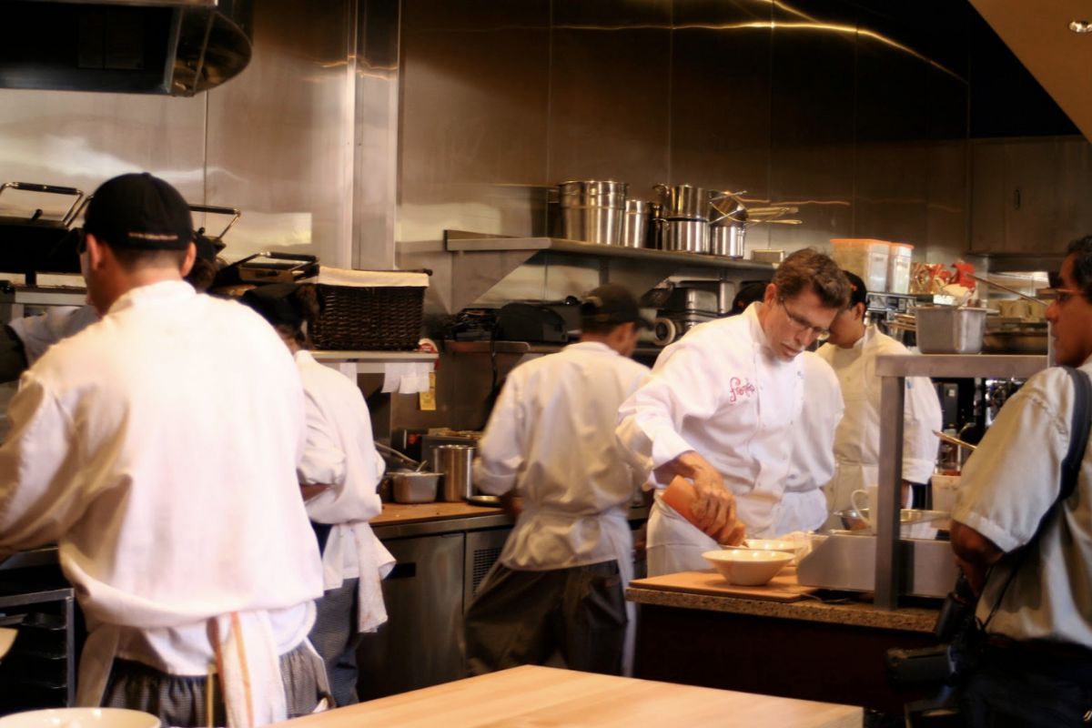 Optima Lakeview® Apartments in Chicago, IL Chefs in white uniforms work together to prepare food in a busy, modern Lakeview dining restaurant kitchen.