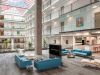 Optima Lakeview® Apartments in Chicago, IL Modern office atrium with blue seating, stylish furniture, glass railings, indoor plants, and a skylight ceiling.