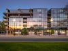 Optima Lakeview® Apartments in Chicago, IL Modern glass apartment building reflecting sunset, showcasing stunning architecture and abundant natural light, with trees and street in front.