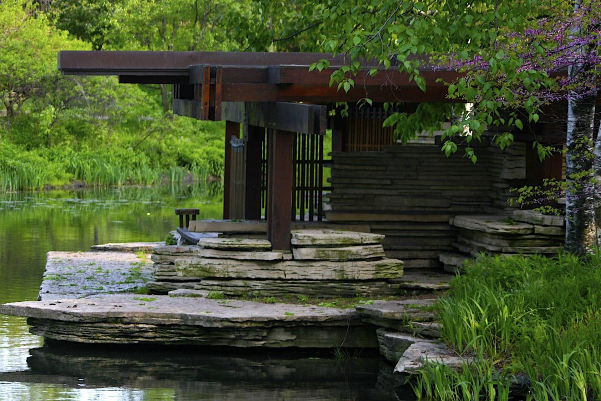 Optima Lakeview® Apartments in Chicago, IL Modern stone and wood pavilion by a pond, inspired by Prairie-Style design, surrounded by lush plants and trees.