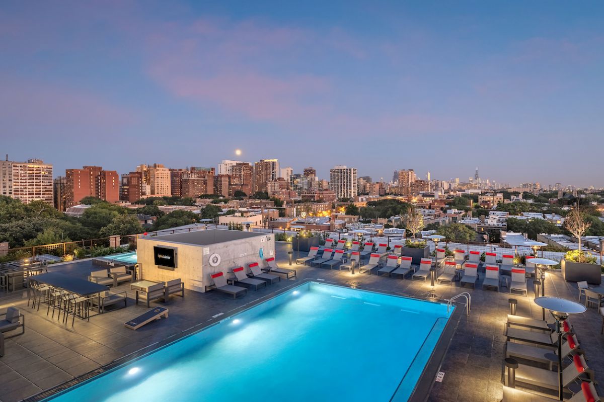 Optima Lakeview® Apartments in Chicago, IL Experience effortless wellness by the rooftop pool as city lights glow and sunset transforms the skyline, lounge chairs inviting pure relaxation.