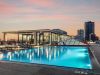Optima Lakeview® Apartments in Chicago, IL Rooftop pool at sunset at Optima Lakeview, with lounge chairs, city skyline, glass building, and tall buildings in the background.