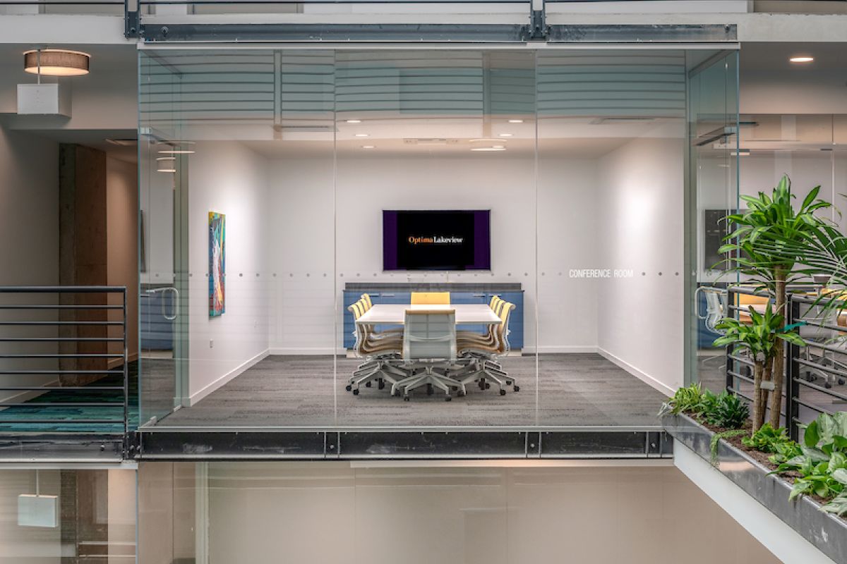 Optima Lakeview® Apartments in Chicago, IL Glass-walled conference room by Optima features modern work design, with chairs, TV, and views of a gym area amidst plants and stylish decor.