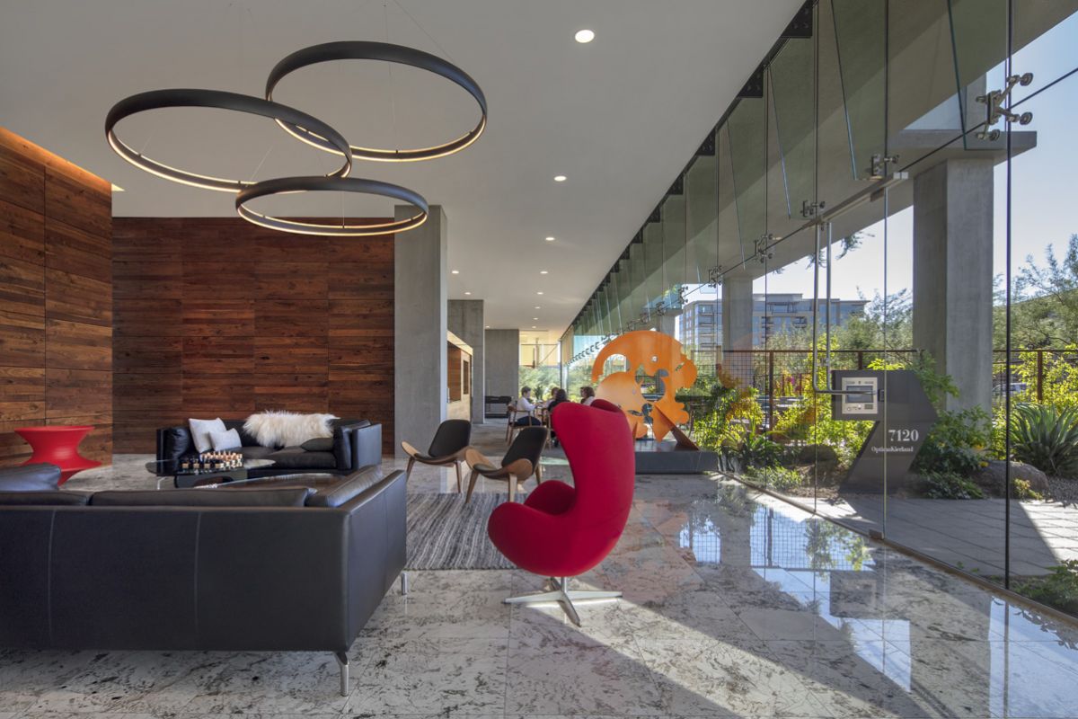 Optima Lakeview® Apartments in Chicago, IL Modern lobby with floor-to-ceiling windows, black sofas, a red chair, and wood accent walls illustrates clever architecture palettes.