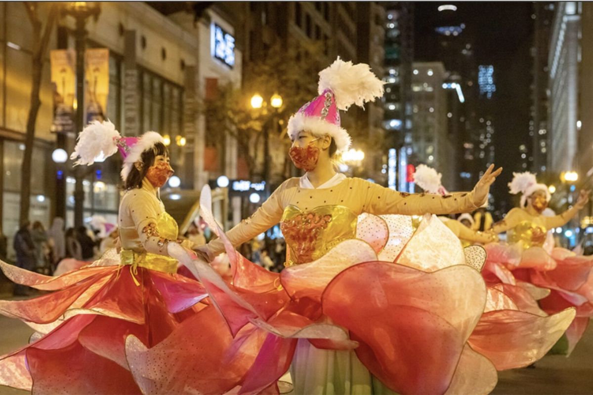 Optima Lakeview® Apartments in Chicago, IL Dancers in bright pink floral costumes and hats perform in the Arts in the Dark Parade under downtown Chicago city lights.