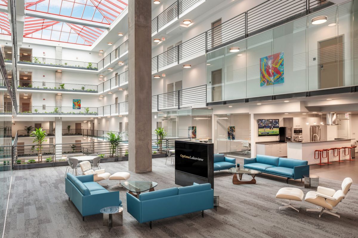 Optima Lakeview® Apartments in Chicago, IL Modern office atrium with blue seating, stylish furniture, glass railings, indoor plants, and a skylight ceiling.