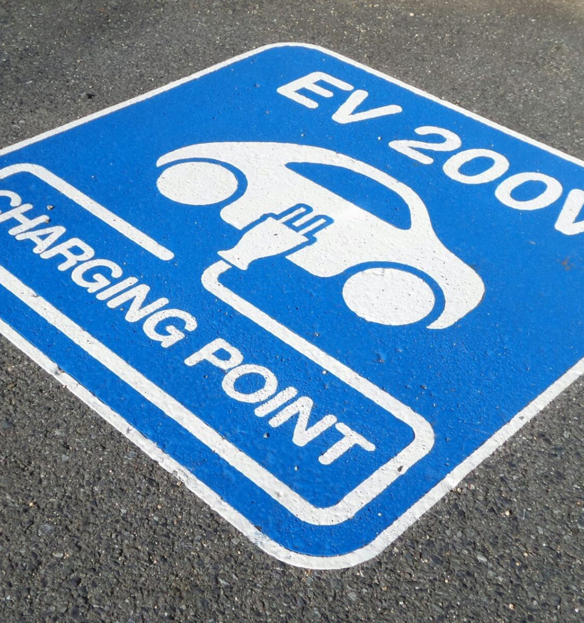 Optima Lakeview® Apartments in Chicago, IL Blue sign on pavement marks EV Parking: "EV 200V Charging Point" with electric car and plug icon, part of the Sustainability Series.