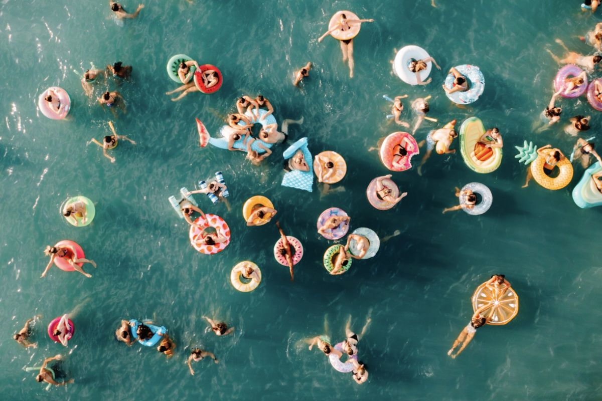 Optima Lakeview® Apartments in Chicago, IL Aerial view of people enjoying a Friday Morning Swim Club, relaxing on colorful pool floats in bright blue water.