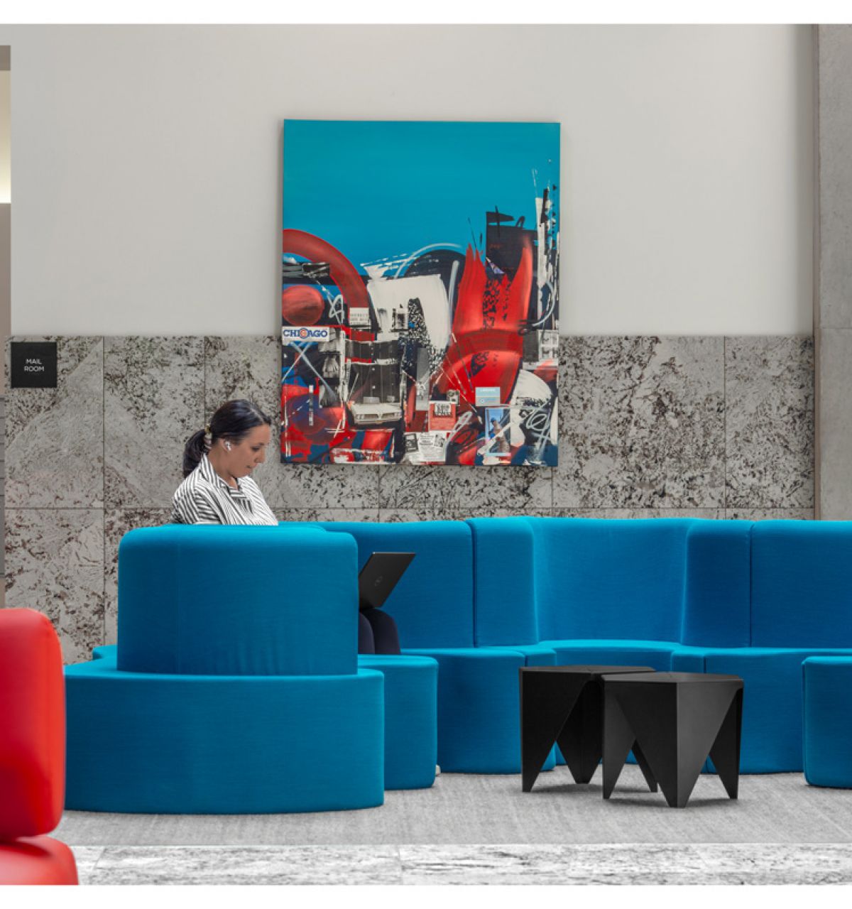 Optima Lakeview® Apartments in Chicago, IL A person works on a laptop while sitting on a blue couch in a modern lobby with colorful artwork on the wall.