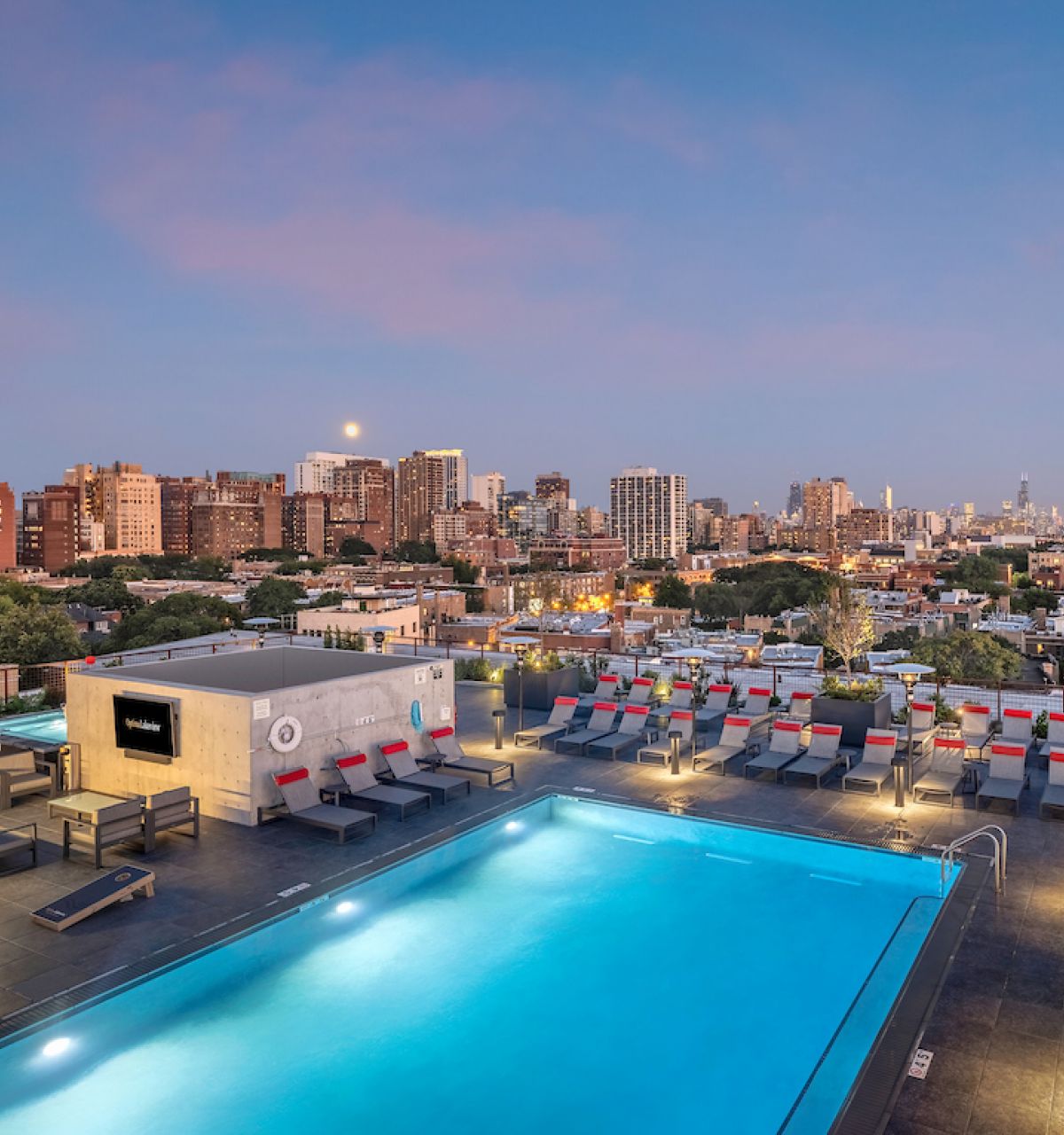 Optima Lakeview® Apartments in Chicago, IL Experience effortless wellness by the rooftop pool as city lights glow and sunset transforms the skyline, lounge chairs inviting pure relaxation.
