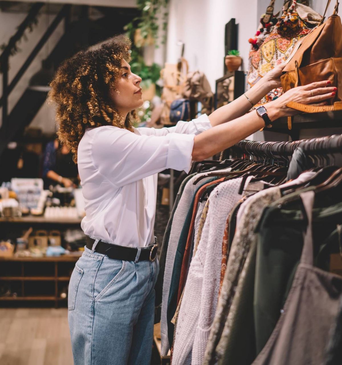 Optima Lakeview® Apartments in Chicago, IL with a woman shopping in a boutique, reaching for a brown bag on a shelf above clothing racks.