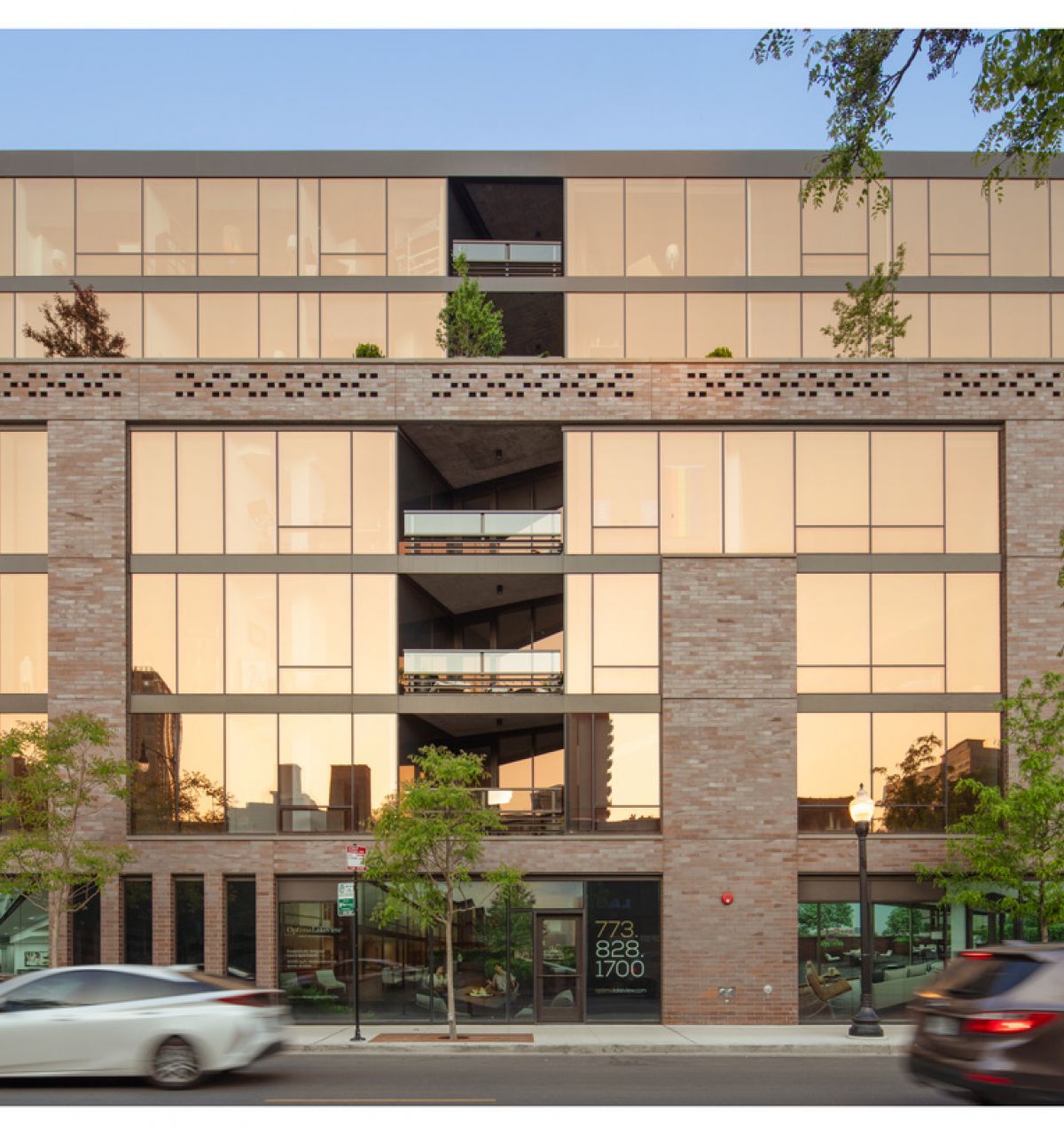 Optima Lakeview® Apartments in Chicago, IL Modern building with large glass windows and brick exterior, cars driving past, and reflections that show our optimized service in the city.
