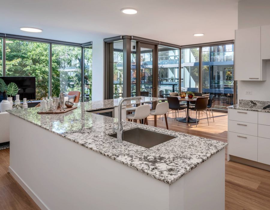 Optima Lakeview® Apartments in Chicago, IL Modern kitchen with granite island, open to dining and living area, large windows, and wood flooring.