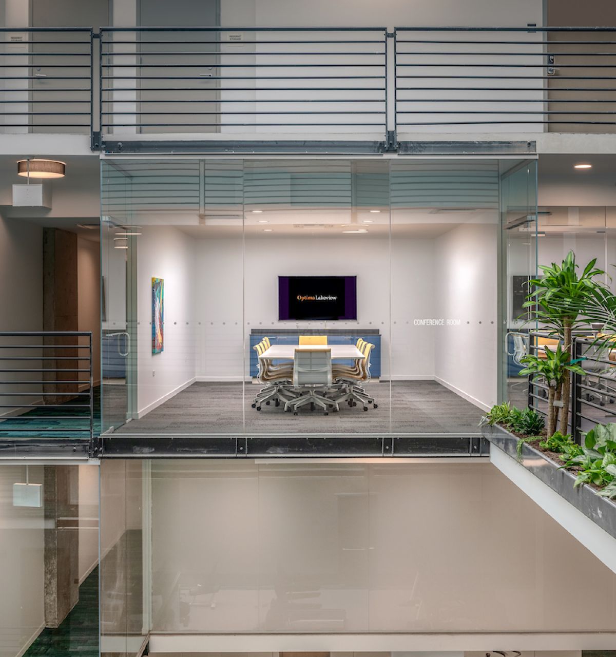 Optima Lakeview® Apartments in Chicago, IL Glass-walled conference room by Optima features modern work design, with chairs, TV, and views of a gym area amidst plants and stylish decor.