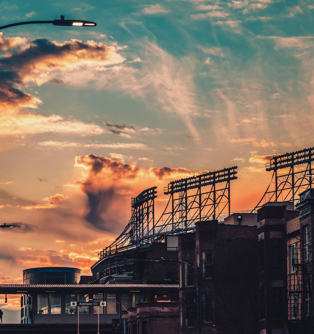 Optima Lakeview® Apartments in Chicago, IL Colorful sunset sky behind a stadium with silhouetted light towers and surrounding city buildings.