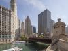 Optima Lakeview® Apartments in Chicago, IL A boat passes under a bridge on the Chicago River, embracing blue space amidst tall city buildings on a sunny day.