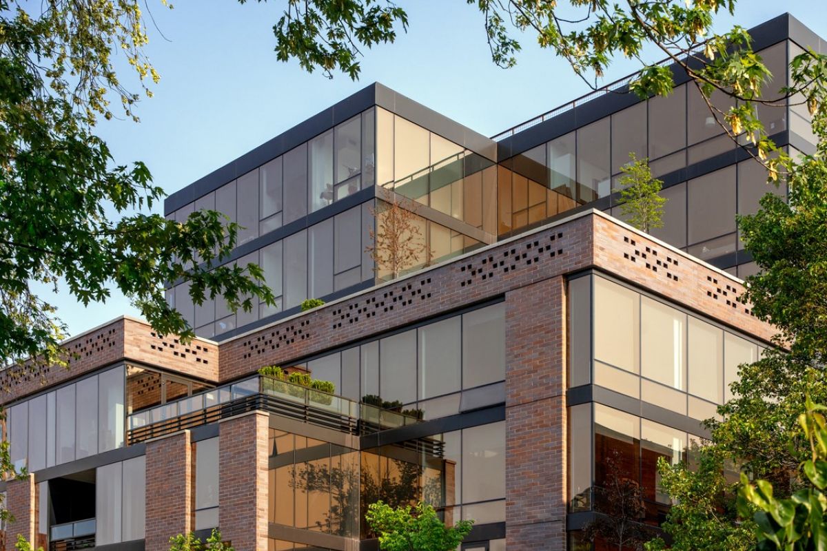 Optima Lakeview® Apartments in Chicago, IL Modern glass and brick apartment building in the Optima Community, surrounded by green trees under a clear blue sky.