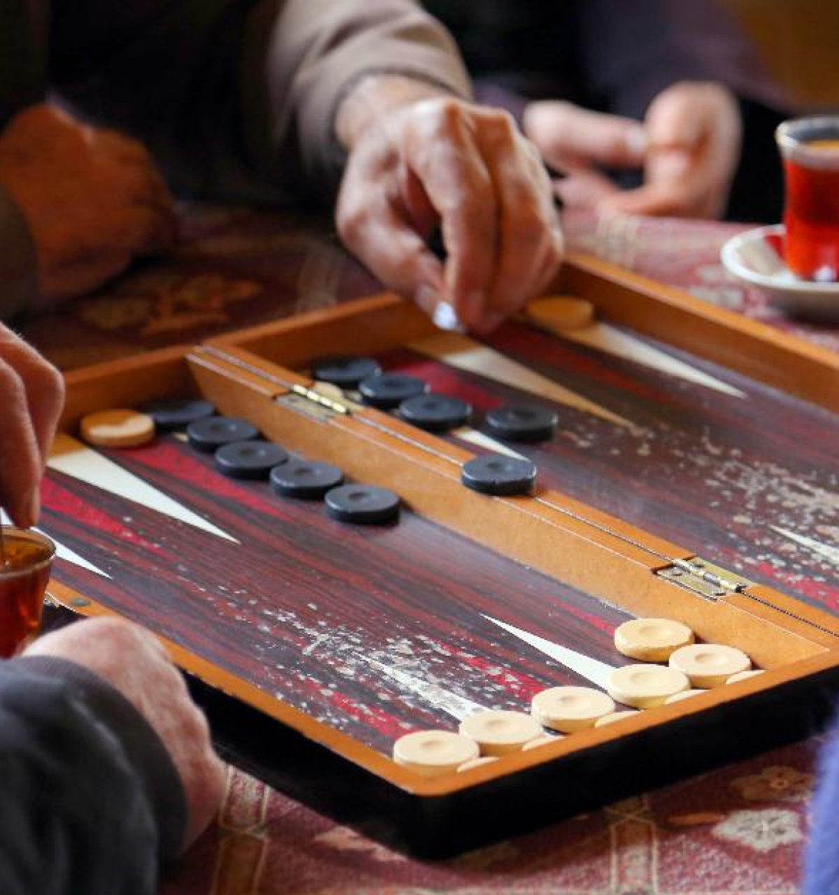Optima Lakeview® Apartments in Chicago, IL Three people enjoy a fun game of backgammon over tea, their hands moving pieces across a trending wooden board.