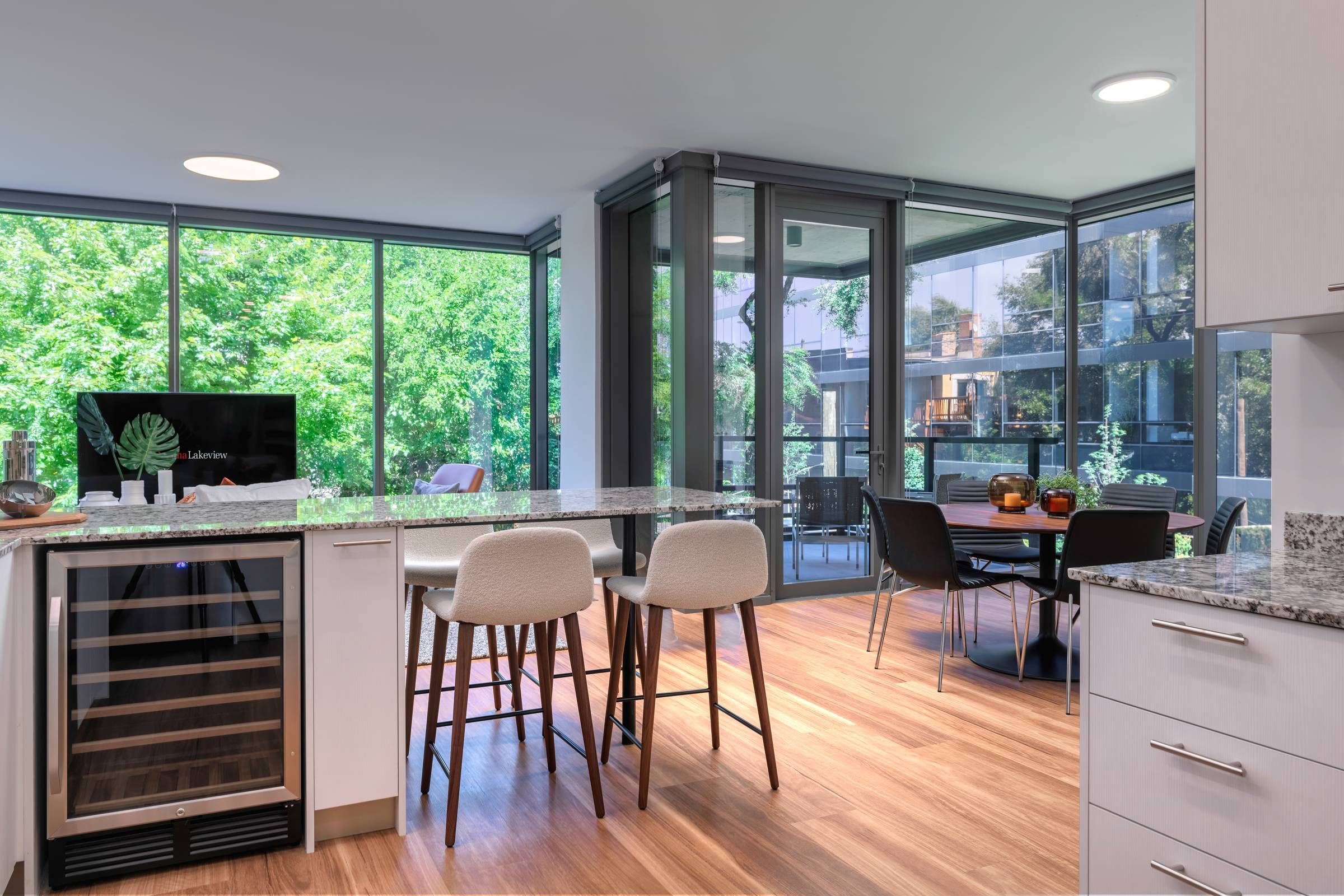 Optima Lakeview® Apartments in Chicago, IL Modern kitchen with island seating, wine fridge, and large windows overlooking trees and a dining area.