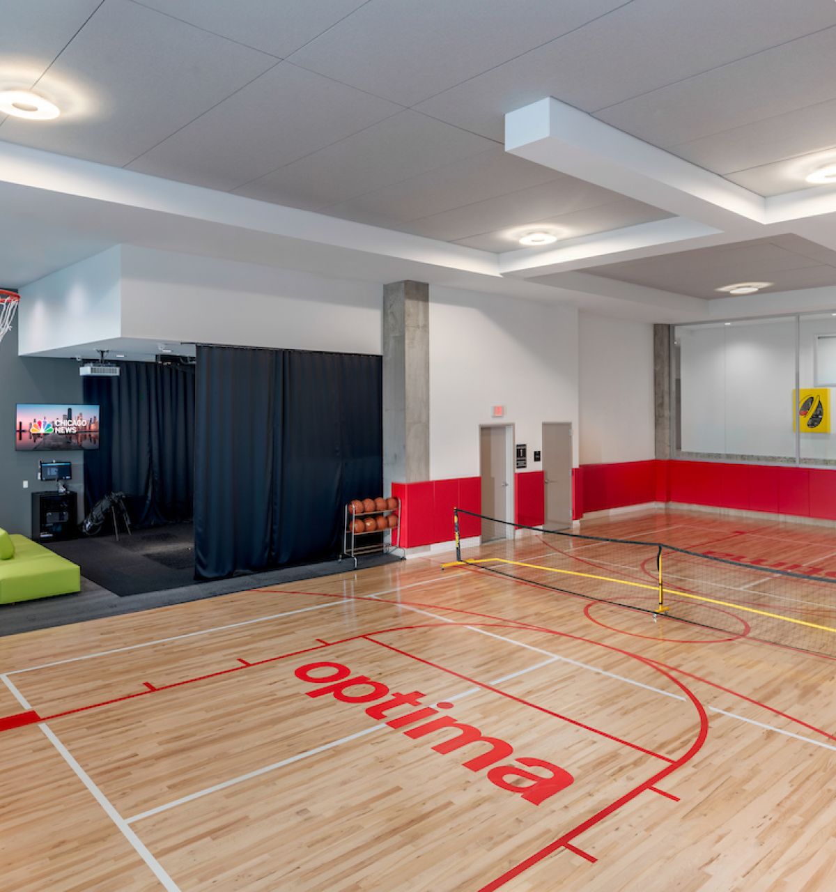 Optima Lakeview® Apartments in Chicago, IL Indoor gym with a basketball court, small tennis net, green couch, and TV in a modern recreational space.