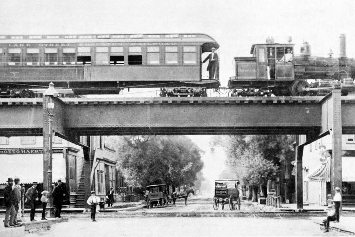 Optima Lakeview® Apartments in Chicago, IL Historic black-and-white photo of a train riding the rails on the Chicago “L” above a bustling street scene.