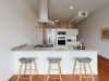 Optima Lakeview® Apartments in Chicago, IL Modern kitchen in Optima Lakeview’s 1B-01 residences features a granite island, three gray stools, and stainless steel appliances.