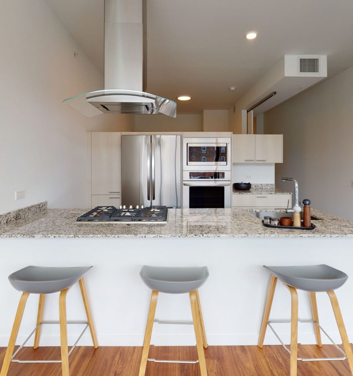 Optima Lakeview® Apartments in Chicago, IL Modern kitchen in Optima Lakeview’s 1B-01 residences features a granite island, three gray stools, and stainless steel appliances.
