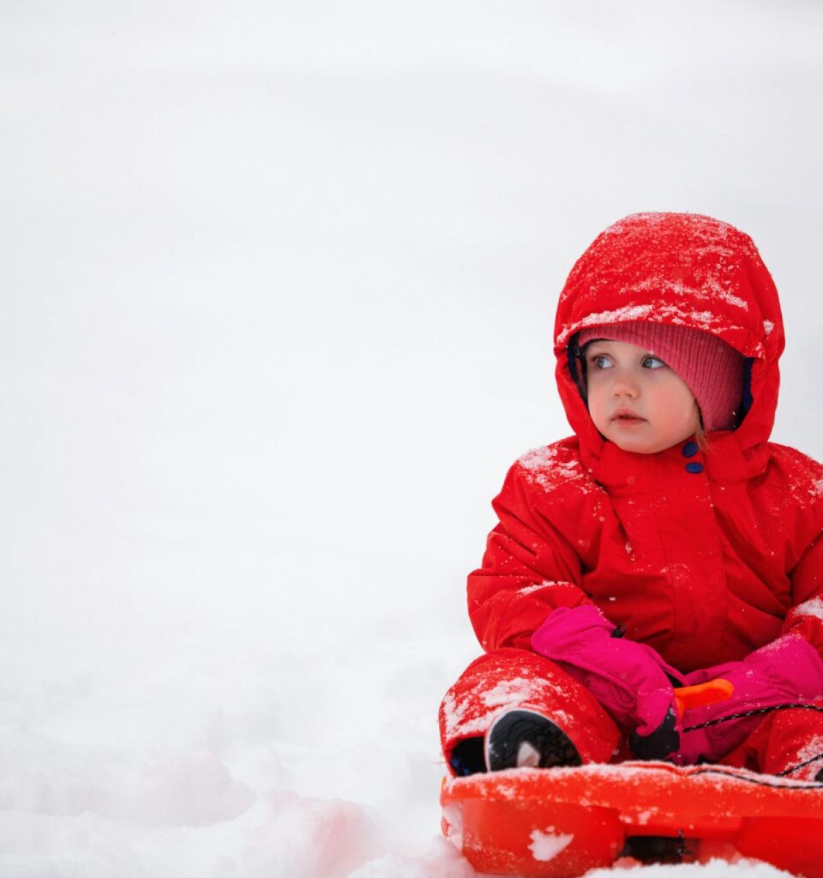 Optima Lakeview® Apartments in Chicago, IL A young child in a red snowsuit sits on a sled, ready for winter fun on the snowy sledding hills.
