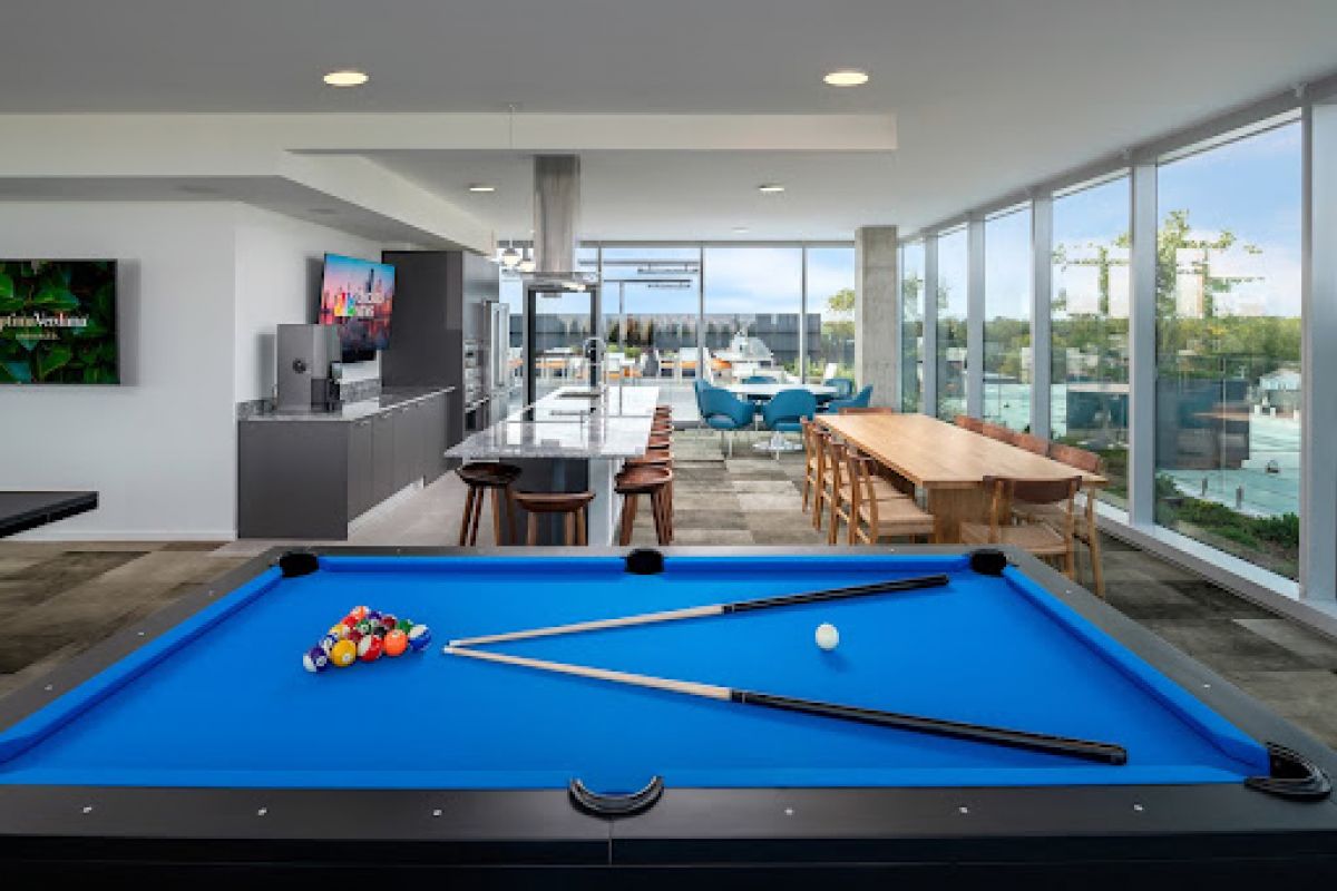 Optima Lakeview® Apartments in Chicago, IL A modern lounge at Optima Lakeview with a billiards table, TV, kitchen, large windows, and city views—perfect for social connections.