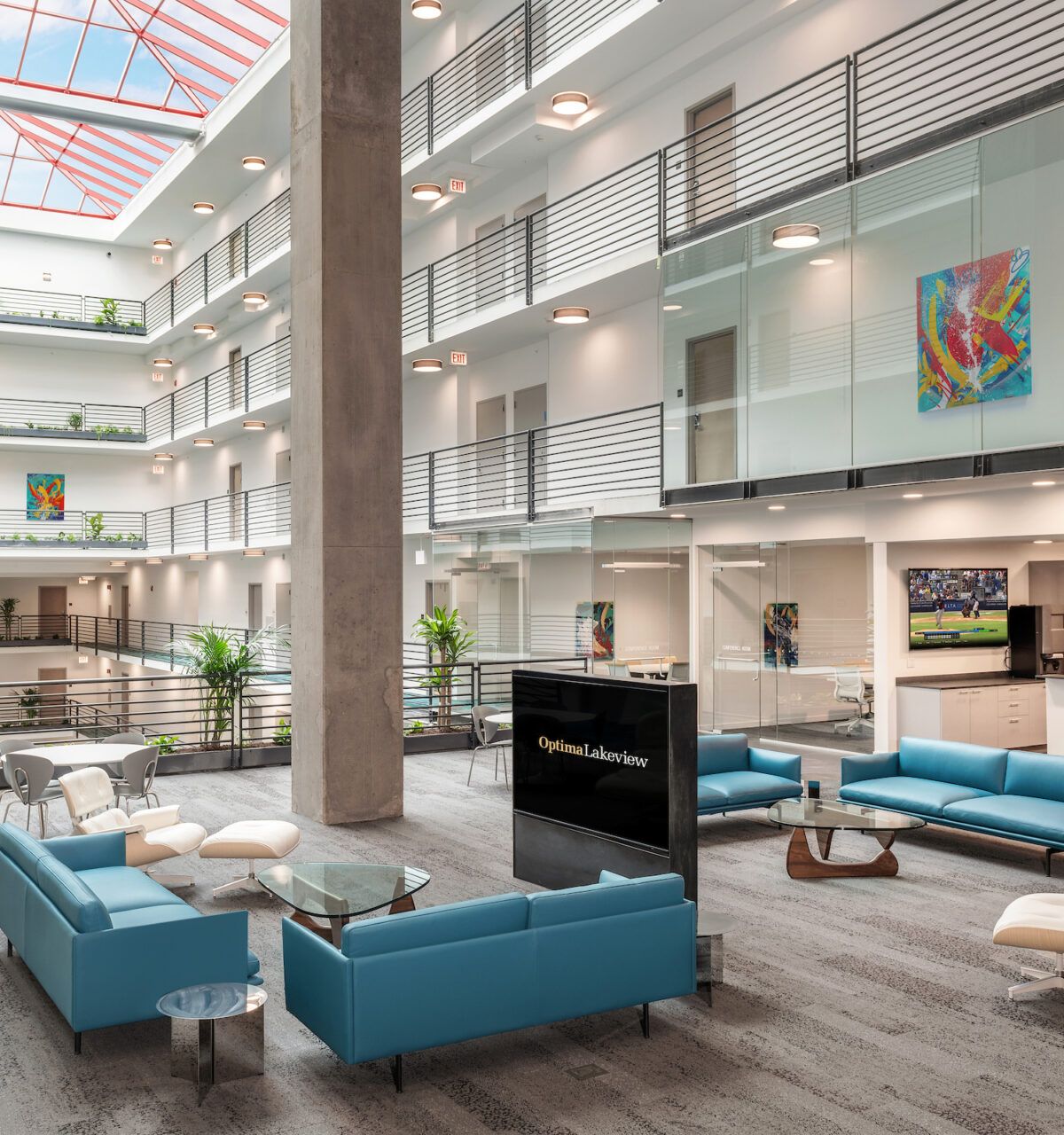 Optima Lakeview® Apartments in Chicago, IL Modern office atrium with blue seating, stylish furniture, glass railings, indoor plants, and a skylight ceiling.