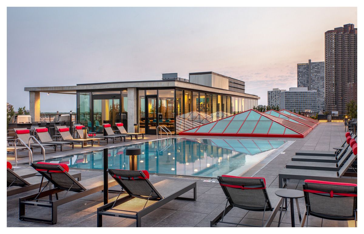 Optima Lakeview® Apartments in Chicago, IL Enjoy stunning evenings on the Sky Deck, featuring a rooftop pool, lounge chairs, red accents, and city views at sunset.