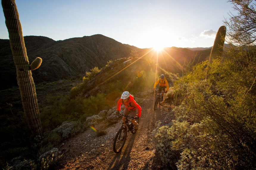 Optima Lakeview® Apartments in Chicago, IL Two cyclists enjoy low-carbon adventure on a desert trail at sunset, surrounded by cacti and rugged hills.