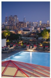 Optima Lakeview® Apartments in Chicago, IL Rooftop pool at dusk with city skyline in the background and lounge chairs surrounding the pool.