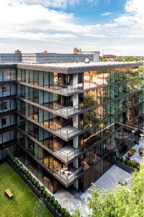 Optima Lakeview® Apartments in Chicago, IL Modern glass apartment building with balconies, featuring green building design and a small courtyard below surrounded by greenery.