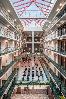 Optima Lakeview® Apartments in Chicago, IL Spacious gym with workout machines under a glass ceiling, surrounded by balconies and modern, sustainable architecture.