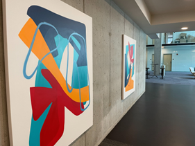Optima Lakeview® Apartments in Chicago, IL Two colorful abstract paintings hang on a concrete wall in a modern, well-lit hallway.