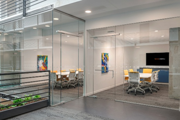 Optima Lakeview® Apartments in Chicago, IL Modern glass-walled conference room with yellow chairs, artwork, and a large screen on the far wall.