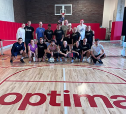 Optima Lakeview® Apartments in Chicago, IL A group celebrates on an indoor pickleball court at Optima Communities, with "optima" proudly displayed on the floor.