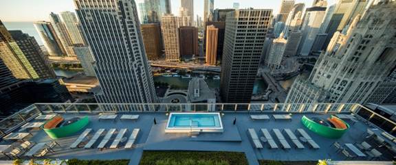 Optima Lakeview® Apartments in Chicago, IL Rooftop pool with lounge chairs overlooking a city skyline—an ideal escape for a good night sleep after exploring the city.